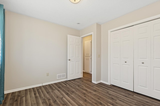 unfurnished bedroom with dark wood finished floors, visible vents, a closet, and baseboards