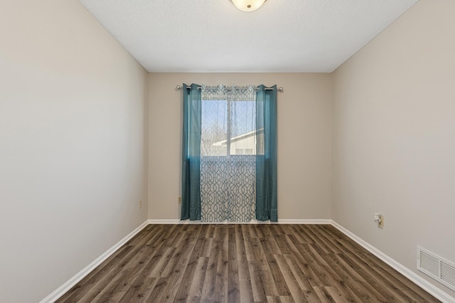 empty room with wood finished floors, visible vents, and baseboards