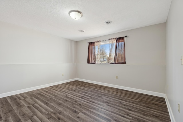 unfurnished room with dark wood-type flooring, visible vents, baseboards, and a textured ceiling