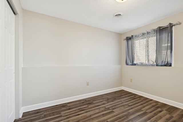 unfurnished room featuring visible vents, baseboards, dark wood-type flooring, and a textured ceiling