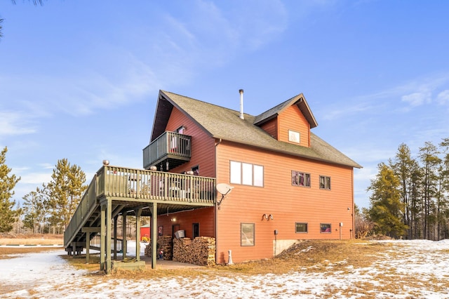 snow covered back of property with a wooden deck and a patio area