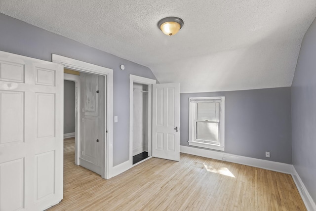 unfurnished bedroom featuring a textured ceiling, a closet, vaulted ceiling, and light wood-type flooring