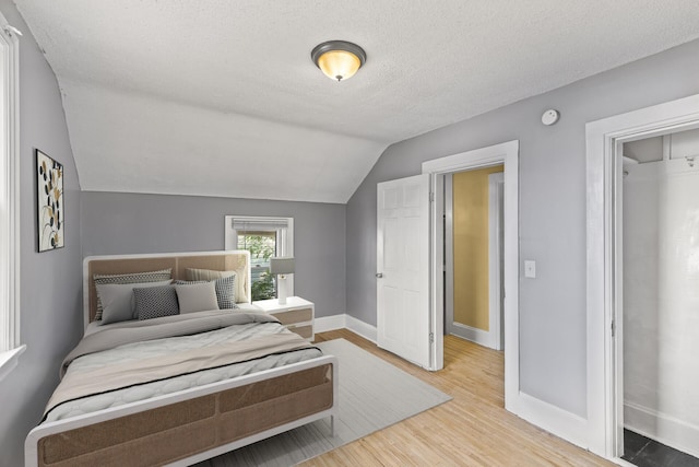 bedroom with a textured ceiling, wood-type flooring, and lofted ceiling