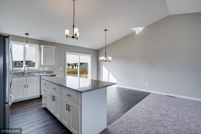 kitchen featuring vaulted ceiling, stainless steel fridge, a notable chandelier, a kitchen island, and white cabinetry