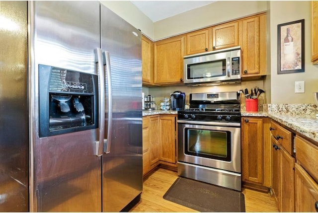 kitchen with light stone counters, light wood-type flooring, and stainless steel appliances