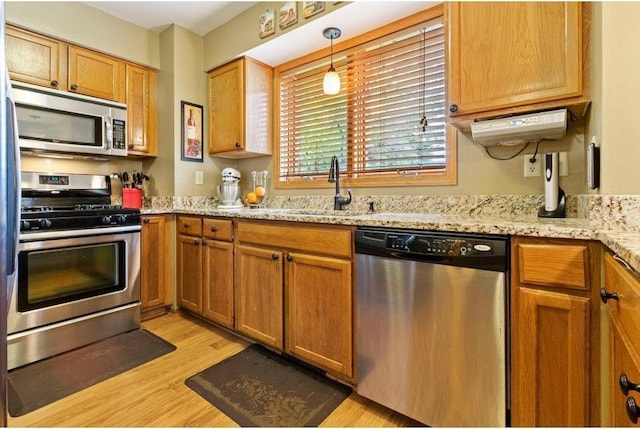 kitchen featuring sink, light stone countertops, light wood-type flooring, decorative light fixtures, and stainless steel appliances