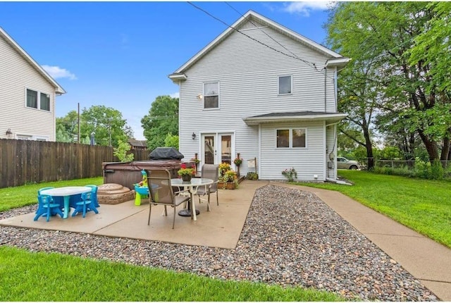 rear view of property featuring a hot tub, a patio area, and a lawn