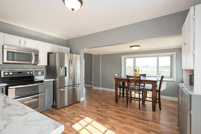 kitchen featuring stainless steel appliances, ornamental molding, white cabinetry, light stone countertops, and light wood-type flooring