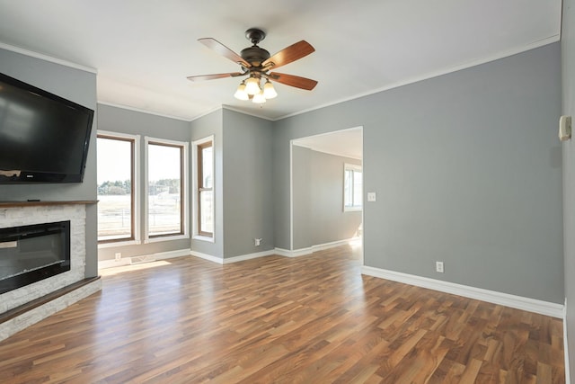 unfurnished living room featuring ceiling fan, a stone fireplace, wood finished floors, baseboards, and crown molding