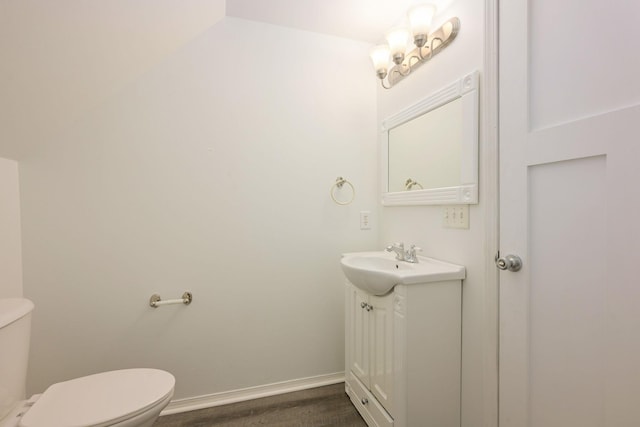 half bath featuring baseboards, vanity, and toilet