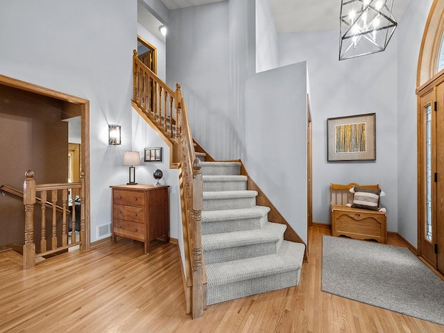 staircase with a high ceiling, hardwood / wood-style floors, and a notable chandelier