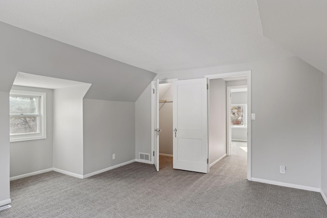 bonus room featuring light colored carpet, a textured ceiling, and lofted ceiling