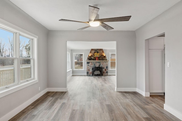 interior space featuring light hardwood / wood-style floors, ceiling fan, and a stone fireplace