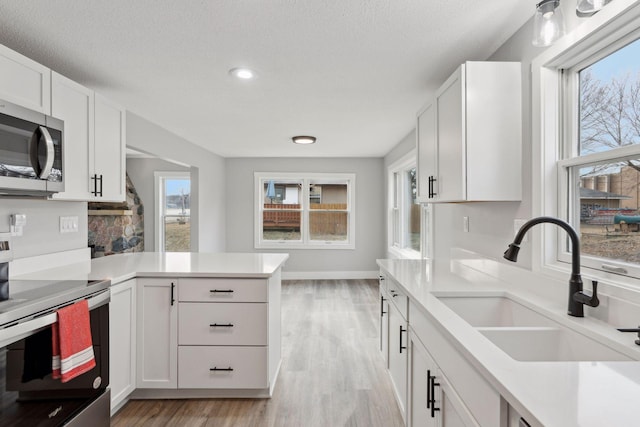 kitchen with white cabinets, stainless steel appliances, sink, kitchen peninsula, and light hardwood / wood-style flooring