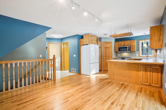 kitchen featuring pendant lighting, backsplash, white refrigerator, kitchen peninsula, and light wood-type flooring