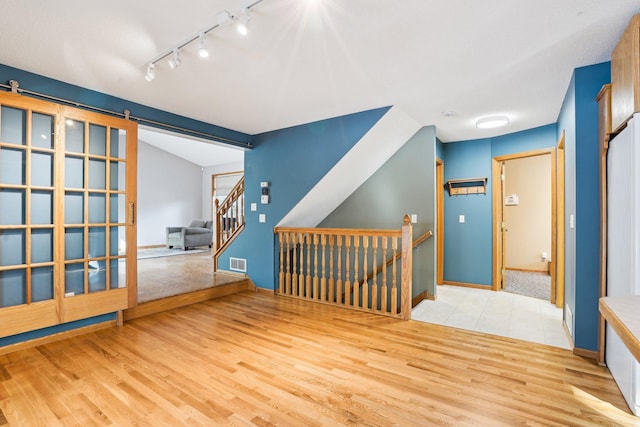 empty room featuring vaulted ceiling, a barn door, and light wood-type flooring