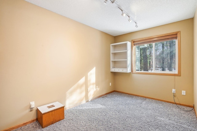 carpeted empty room with track lighting and a textured ceiling