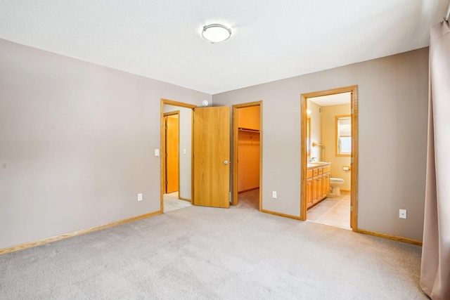 unfurnished bedroom with sink, a spacious closet, light colored carpet, ensuite bath, and a closet