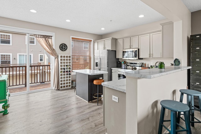 kitchen featuring kitchen peninsula, appliances with stainless steel finishes, a kitchen breakfast bar, and a textured ceiling