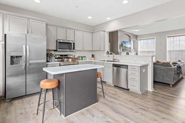 kitchen featuring a kitchen bar, stainless steel appliances, a kitchen island, light hardwood / wood-style flooring, and sink