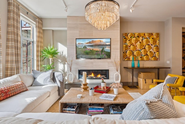 living room with light hardwood / wood-style floors, a large fireplace, track lighting, and an inviting chandelier