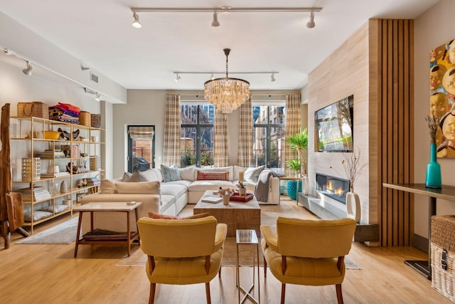 living area with a premium fireplace, light hardwood / wood-style flooring, and a notable chandelier