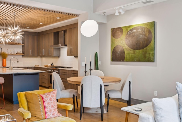 interior space featuring tasteful backsplash, light wood-type flooring, hanging light fixtures, wall chimney range hood, and sink