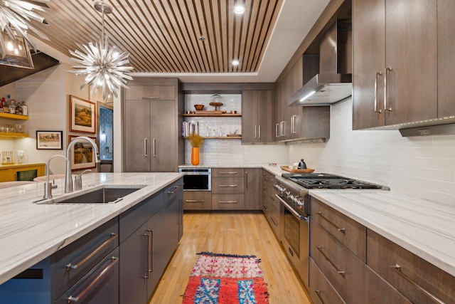 kitchen featuring a notable chandelier, wall chimney range hood, sink, dark brown cabinetry, and stainless steel appliances