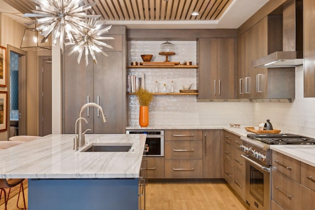 kitchen featuring wall chimney range hood, sink, an island with sink, and stainless steel appliances