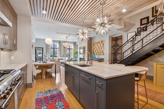 kitchen featuring high end stove, decorative light fixtures, a kitchen island with sink, a breakfast bar, and sink