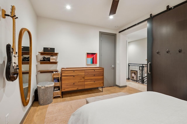 bedroom with ceiling fan, a barn door, and light wood-type flooring