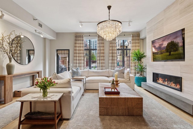 living area with track lighting, visible vents, wood finished floors, a fireplace, and a notable chandelier