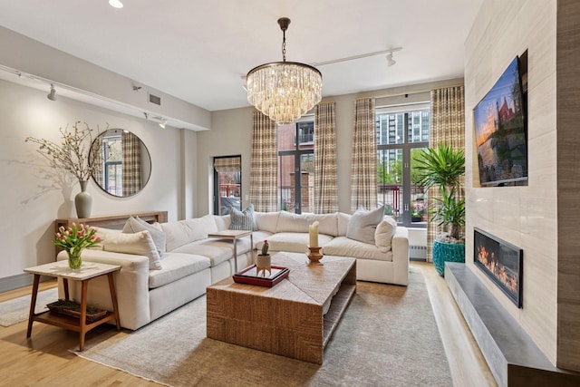 living room featuring a notable chandelier, track lighting, a tiled fireplace, wood finished floors, and visible vents