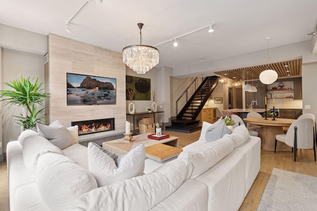 living room featuring track lighting, wood finished floors, stairway, a tile fireplace, and a notable chandelier