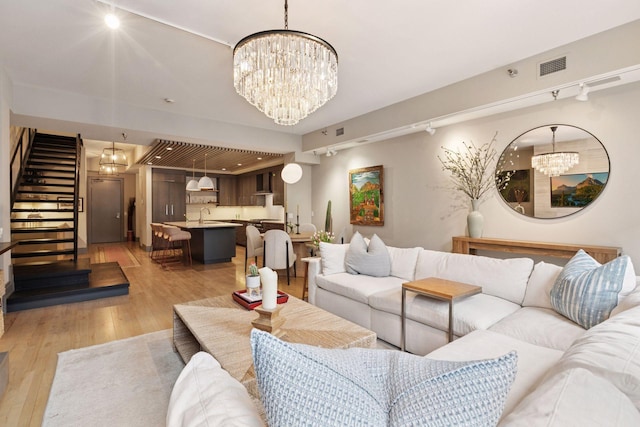 living room featuring visible vents, stairs, light wood-type flooring, rail lighting, and a notable chandelier