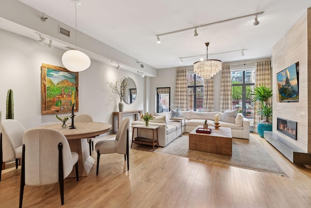 living room featuring track lighting, light wood finished floors, a chandelier, a tiled fireplace, and visible vents