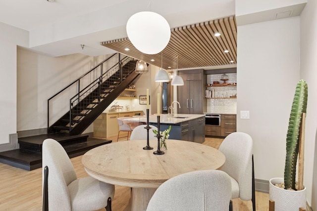 dining room featuring light wood-style floors, recessed lighting, wet bar, and stairs