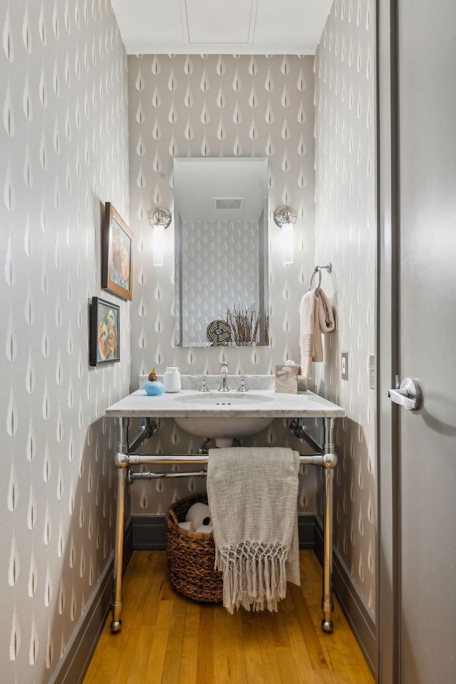 bathroom with a sink, baseboards, wood-type flooring, and wallpapered walls