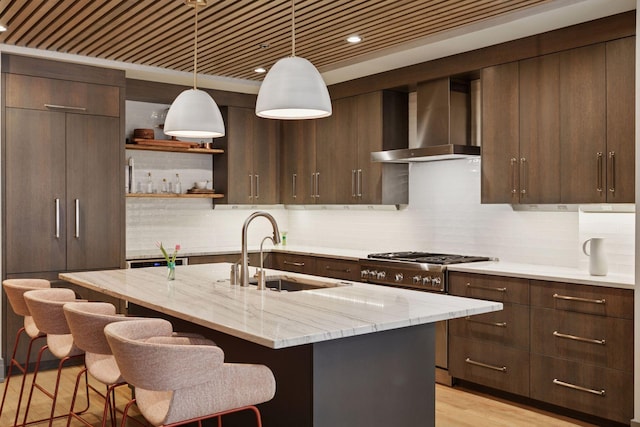 kitchen featuring dark brown cabinetry, a kitchen bar, gas range oven, wall chimney exhaust hood, and a sink