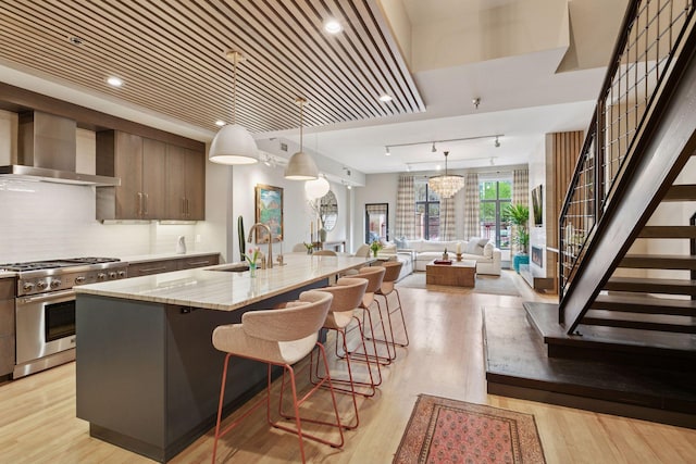 kitchen with a kitchen island with sink, a kitchen bar, high end stove, a sink, and wall chimney exhaust hood