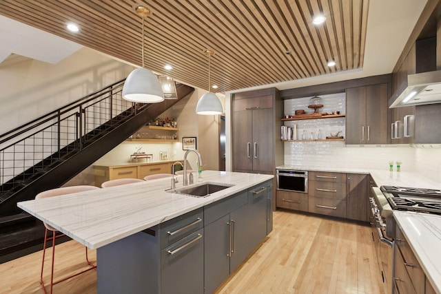 kitchen featuring open shelves, a sink, wall chimney exhaust hood, light wood-type flooring, and high end stainless steel range oven
