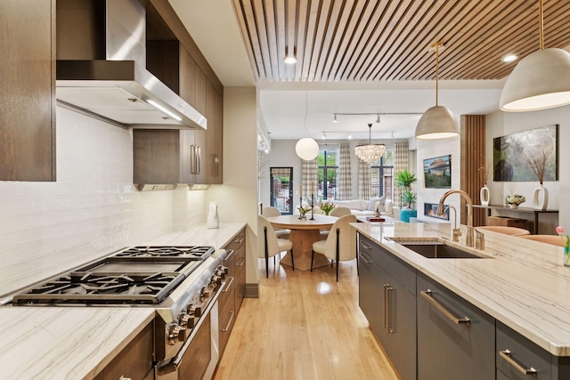 kitchen featuring light stone countertops, open floor plan, light wood-type flooring, wall chimney exhaust hood, and a sink