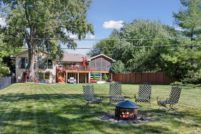 view of yard featuring a wooden deck, a sunroom, a fire pit, and fence