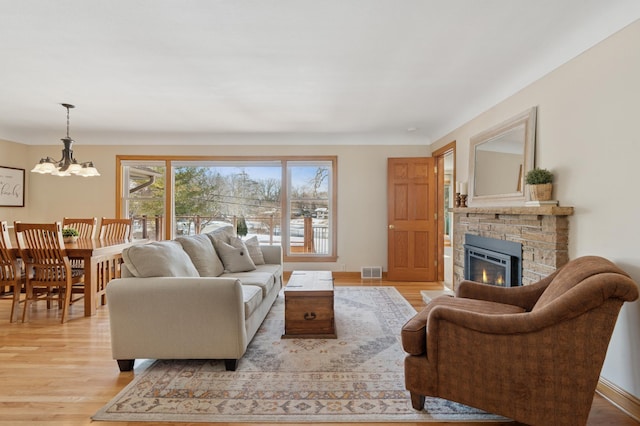 living area featuring baseboards, visible vents, a stone fireplace, light wood-style floors, and a chandelier