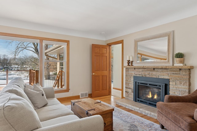 living room featuring a fireplace, wood finished floors, visible vents, and baseboards