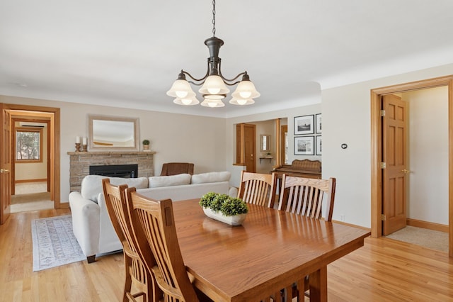 dining space featuring baseboards, a fireplace, light wood-type flooring, and a chandelier