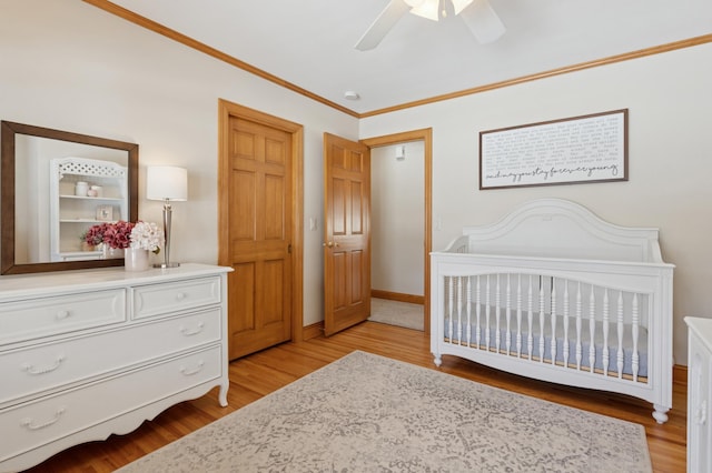 bedroom with a ceiling fan, baseboards, light wood finished floors, ornamental molding, and a crib