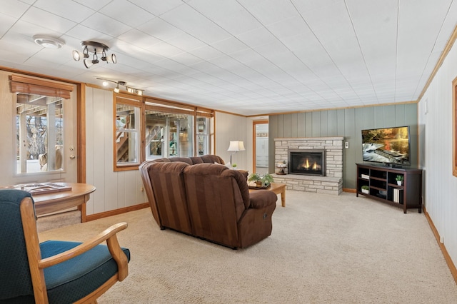 living room featuring baseboards, a stone fireplace, ornamental molding, and carpet flooring