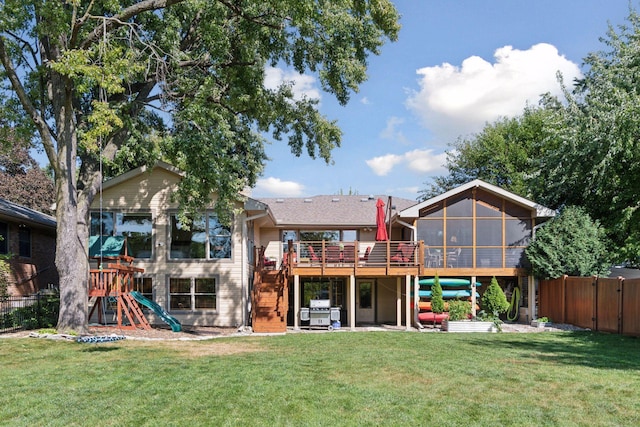 rear view of property featuring stairway, fence, a yard, a sunroom, and a deck