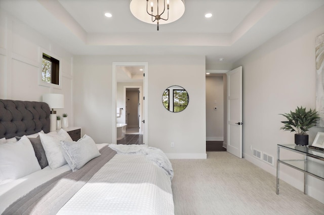 bedroom with a raised ceiling, light colored carpet, and ensuite bath